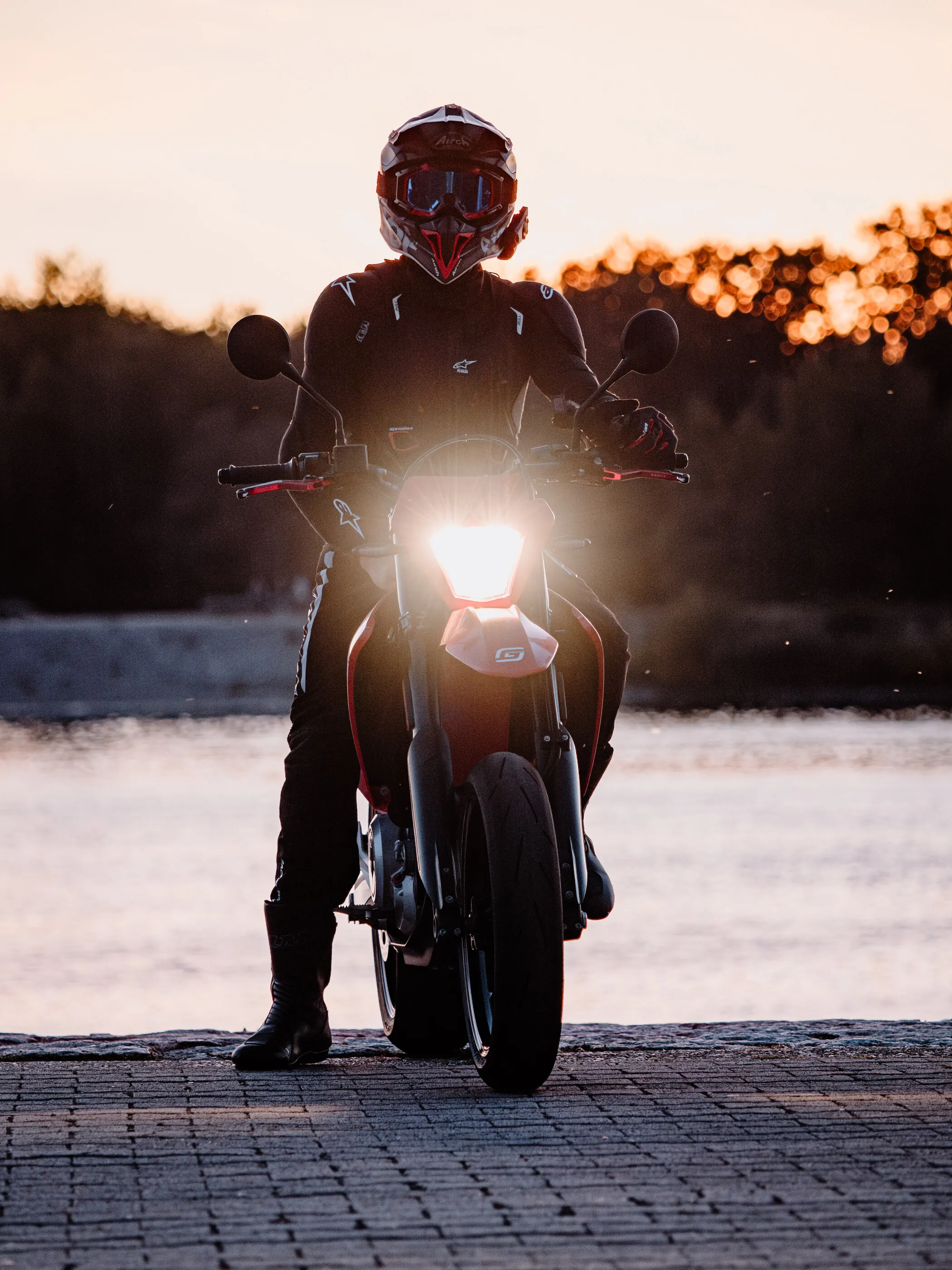 Motorradfahrer mit eingeschaltetem Scheinwerfer im Sonnenuntergang am See