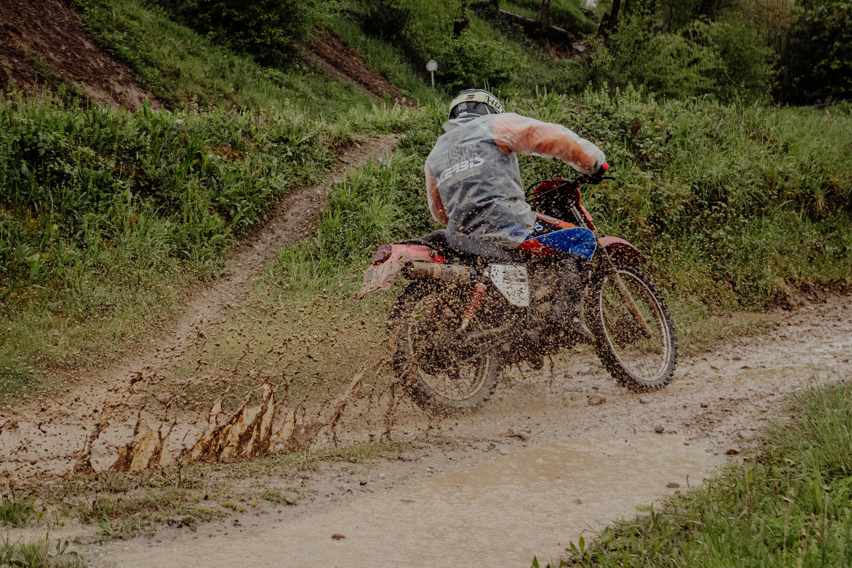 Enduro-Fahrer in der Kurve, Schlamm spritzt vom Hinterrad
