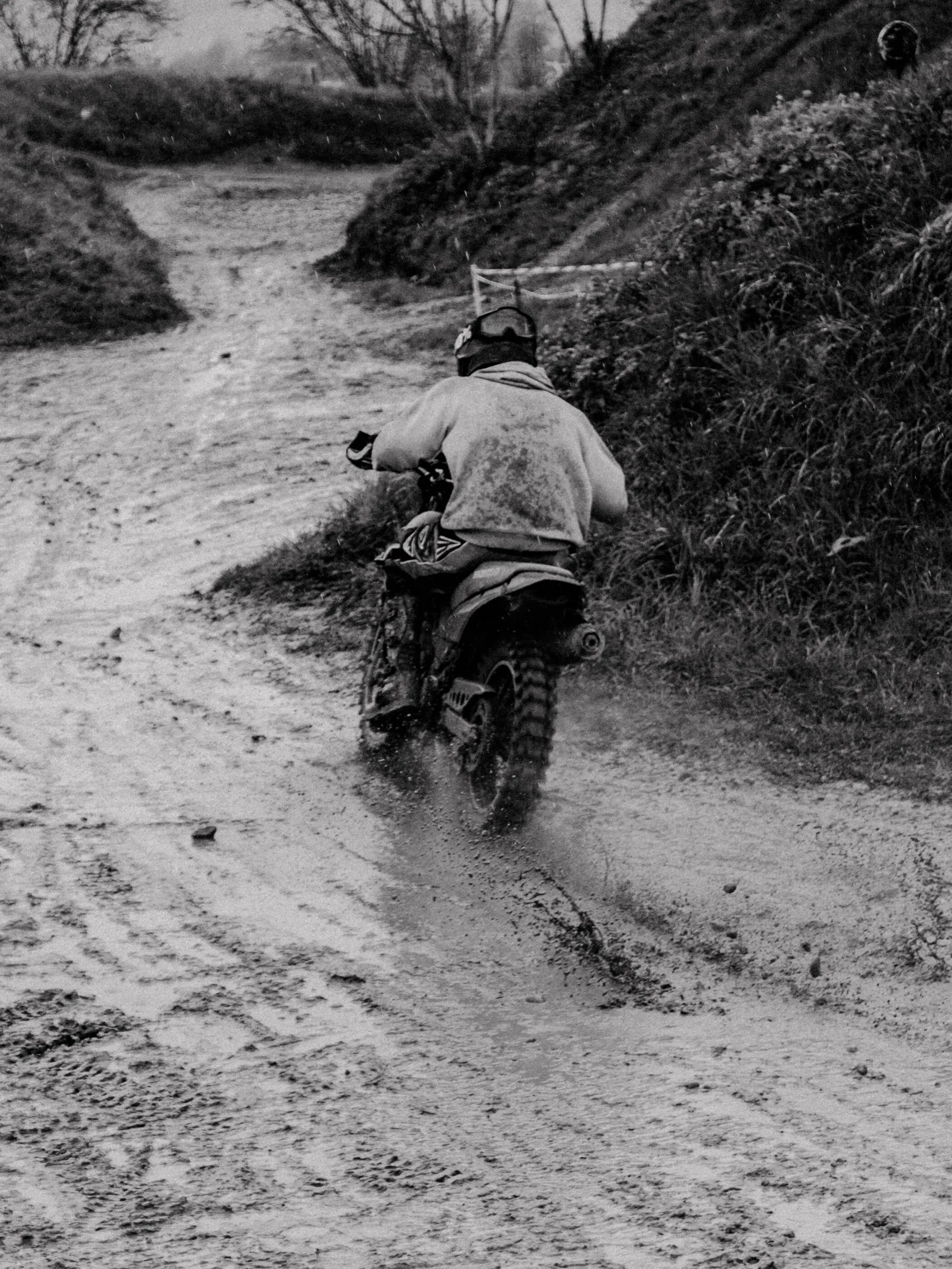 Schwarz-Weiß-Aufnahme eines Enduro-Fahrers auf schlammiger Strecke im Regen